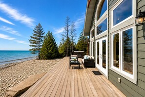 A wooden deck with outdoor furniture, a hot tub, and a view of the sea and trees.