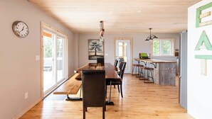 Un comedor amplio con una mesa y sillas de madera, una cocina con barra y un ventanal que proporciona luz natural.