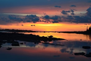 A sunset over a calm lake with rocks in the foreground and a forested shoreline.