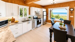 Une cuisine moderne avec des meubles blancs, un réfrigérateur en acier inoxydable et un coin repas offrant une vue sur la plage.