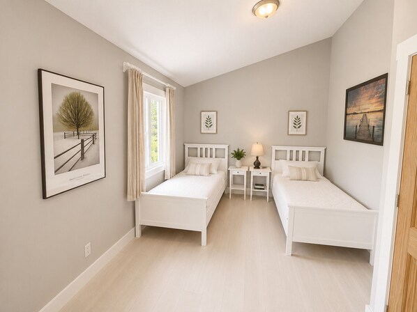Une chambre avec deux lits, une fenêtre avec des rideaux, une table de chevet avec une lampe et des œuvres d’art encadrées accrochées aux murs.