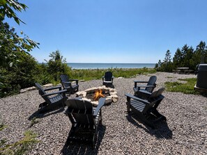 Un espace aménagé près de la plage, avec quatre fauteuils Adirondack disposés autour d’un foyer, offrant une vue sur l’océan.