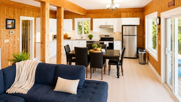 Une cuisine moderne avec des meubles blancs, un réfrigérateur en acier inoxydable et un coin repas comprenant une table et des chaises.