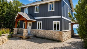 Une maison à deux étages, avec des fondations en pierre, un porche en bois et une vue sur l’eau.