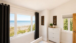 Une chambre avec vue sur la plage, une commode blanche et un lit recouvert d’une couverture à rayures.