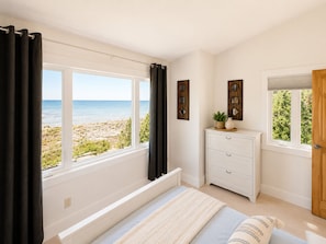 Ein Schlafzimmer mit Blick auf den Strand, eine weiße Kommode und ein Bett mit gestreifter Decke.