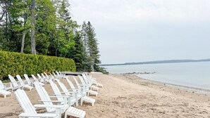 Une plage avec des chaises longues blanches disposées en rangées, un rivage sablonneux et une mer calme en arrière-plan.
