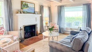 Un salon chaleureux avec une cheminée, des meubles en osier, un canapé et une vue sur l’extérieur.