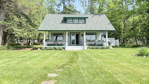 Une maison de plain-pied avec un toit végétalisé et des éléments décoratifs blancs, entourée d’une pelouse bien entretenue et d’arbres.