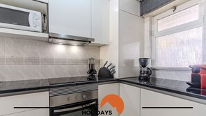 Cocina moderna con armarios blancos, microondas integrado, estufa y cafetera.