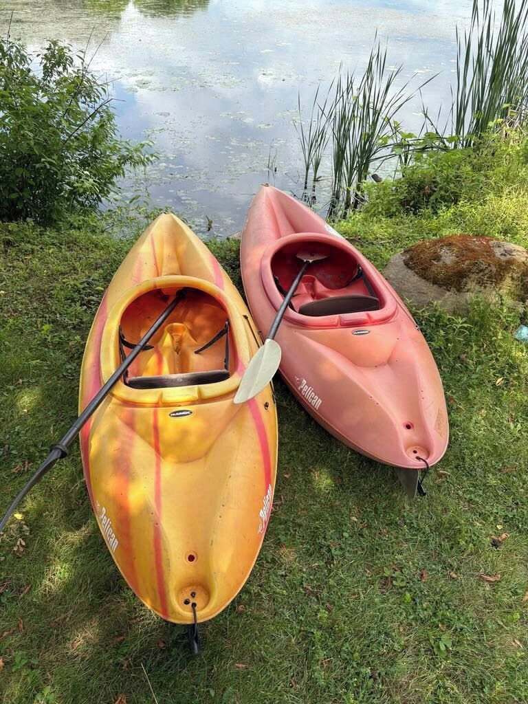 Two kayaks on grass near a body of water.