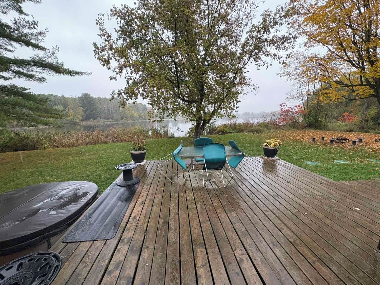 Une terrasse en bois avec une table et des chaises, d’où l’on peut admirer un lac et les couleurs automnales des arbres.