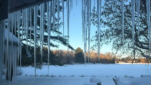 Lumipeitteinen ulkoalue, jonka katosta roikkuu jääpuikkoja, sekä penkki ja pöytä.