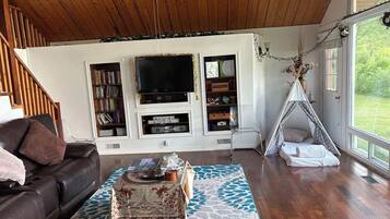 A living room with a wooden ceiling, a TV, bookshelves, a sofa, a coffee table, and a teepee.