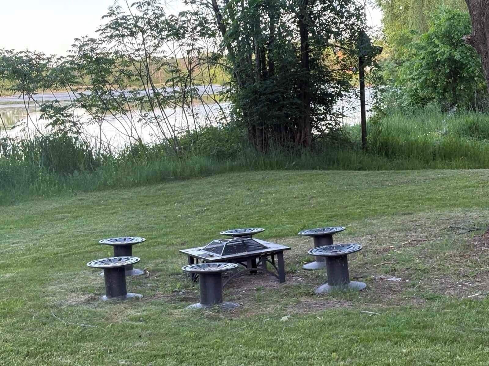 Zona exterior amb gespa, una taula i cadires, envoltada d'arbres i una massa d'aigua.