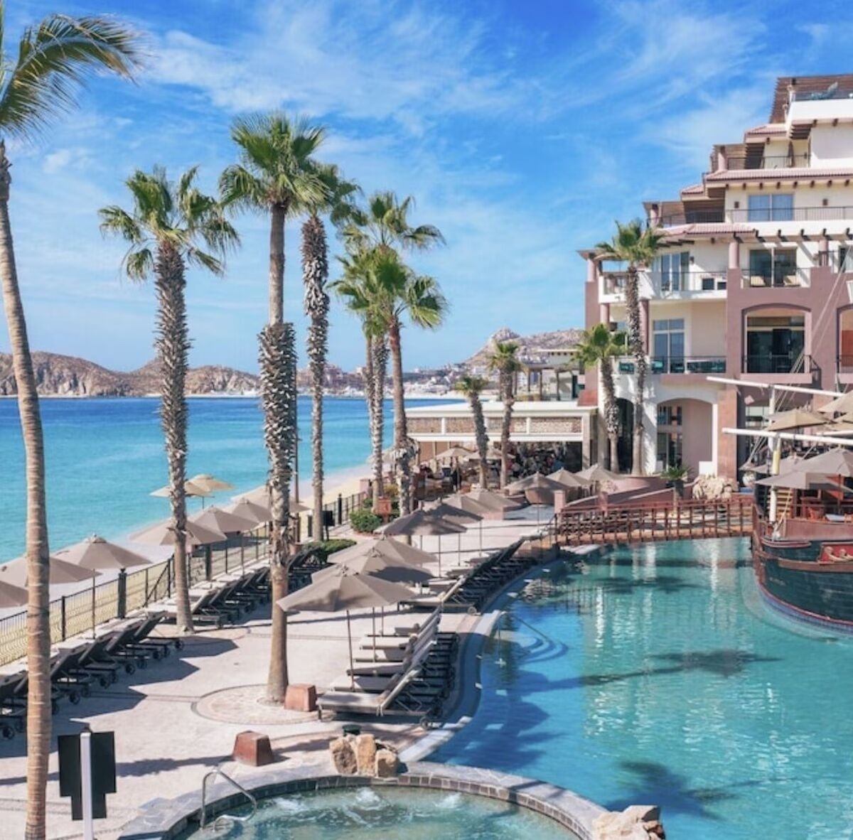 A resort with a pool area, palm trees, and a view of the sea.