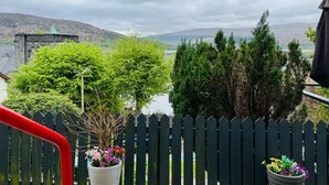 A view from a balcony with a wooden fence, a potted plant, and a distant view of a building and hills.