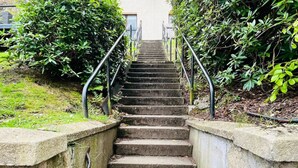 A concrete staircase with metal railings, surrounded by greenery.