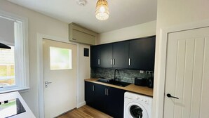 A compact kitchen with dark cabinets, a washing machine, and a window.