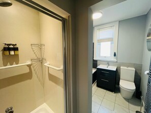 A bathroom with a shower, toilet, sink, and storage cabinets.