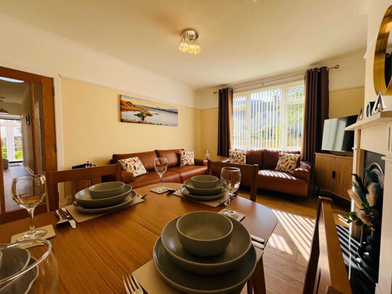 A dining area with a wooden table set for four, a brown leather sofa, and a painting on the wall.