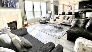 Un salón comedor espacioso con chimenea, ventanas amplias y una cocina moderna al fondo.