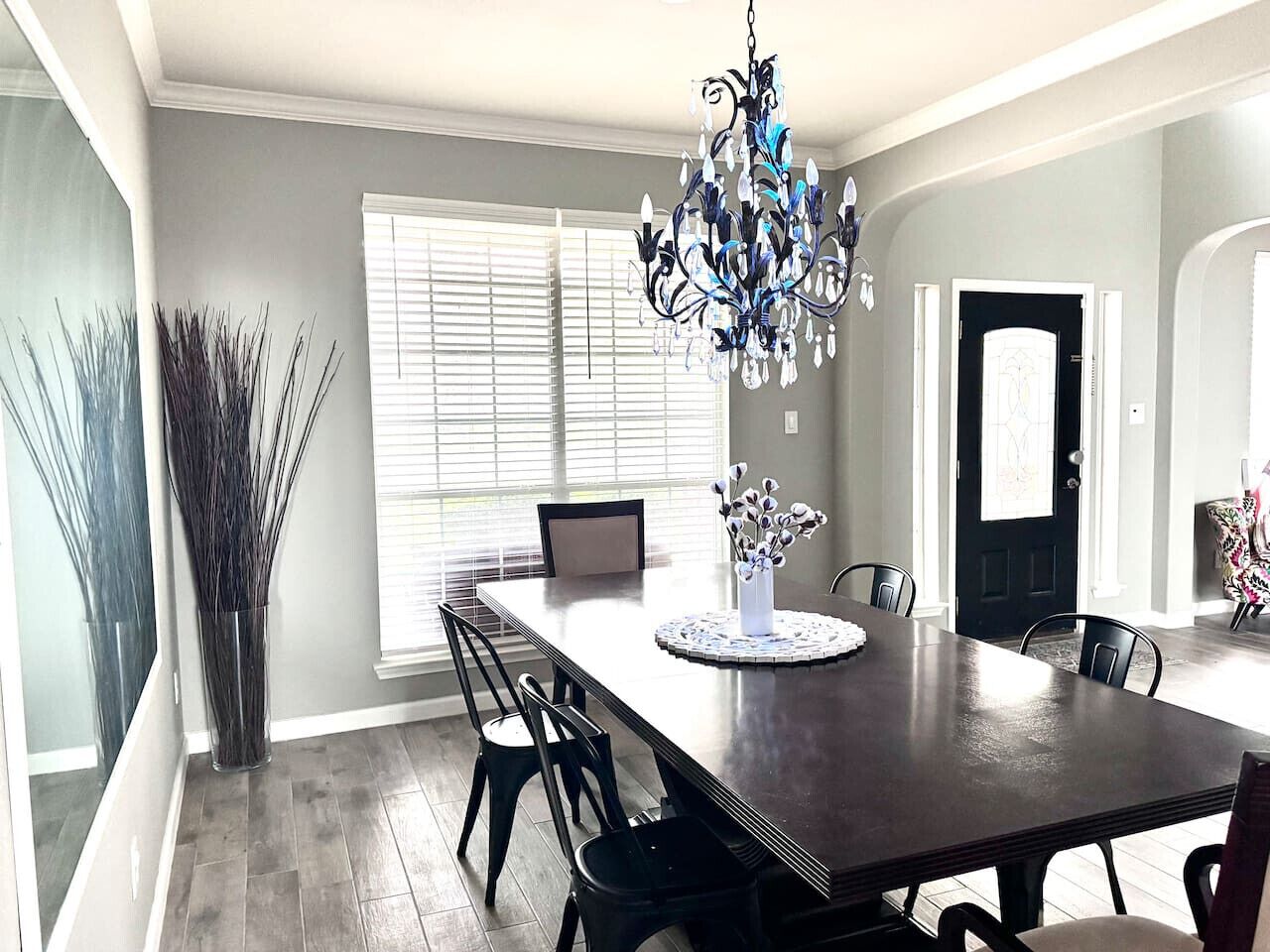 A dining room with a dark wooden table, chairs, a chandelier, and a vase with branches.