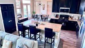 Una cocina moderna con armarios oscuros, una isla central con taburetes y un comedor con mesa y sillas.
