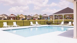 A swimming pool with lounge chairs, a covered seating area, and a row of townhouses in the background. - The Cottages 3  2BR2BA Dothan Pet Friendly Gorgeous Pool, Pickle Ball court, Gym (Dothan)