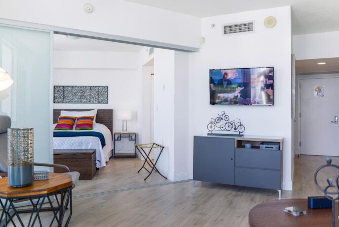 A modern hotel room with a bed, bedside table, lamp, and a television mounted on the wall.