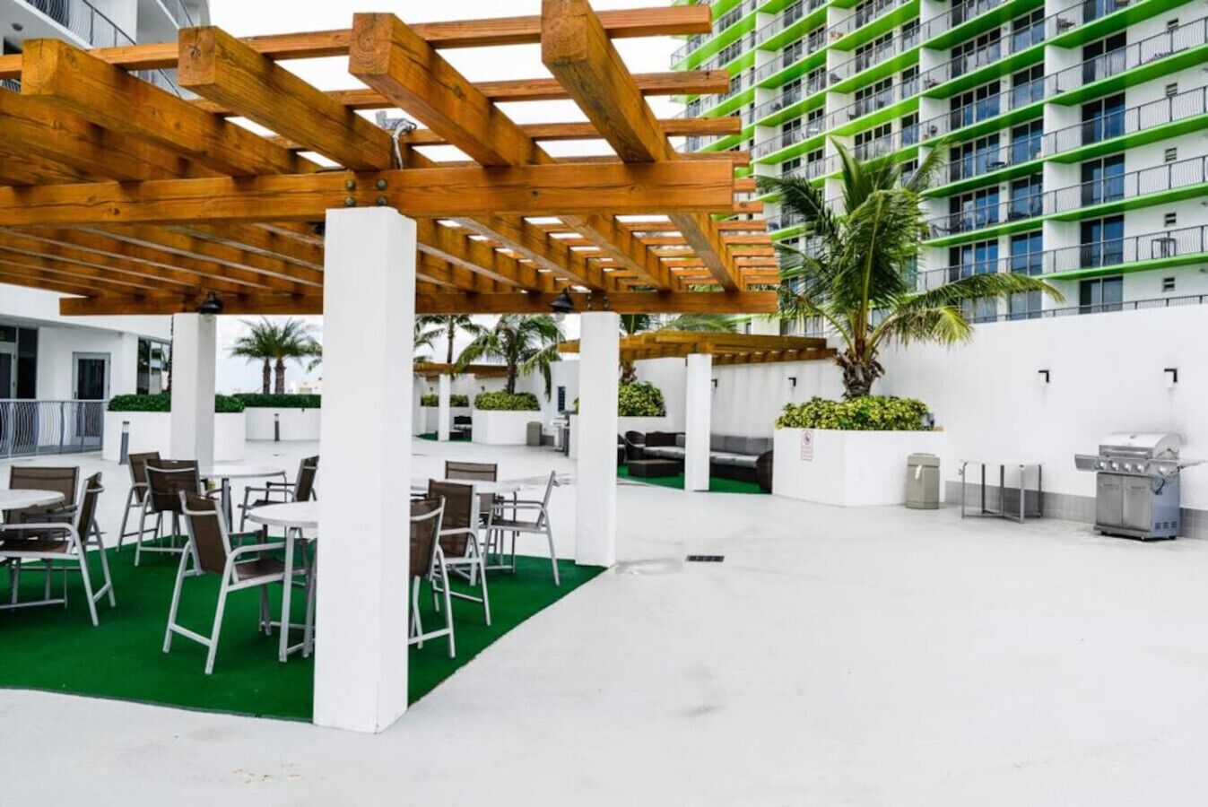 An outdoor patio area with tables and chairs, a grill, and a pergola structure.