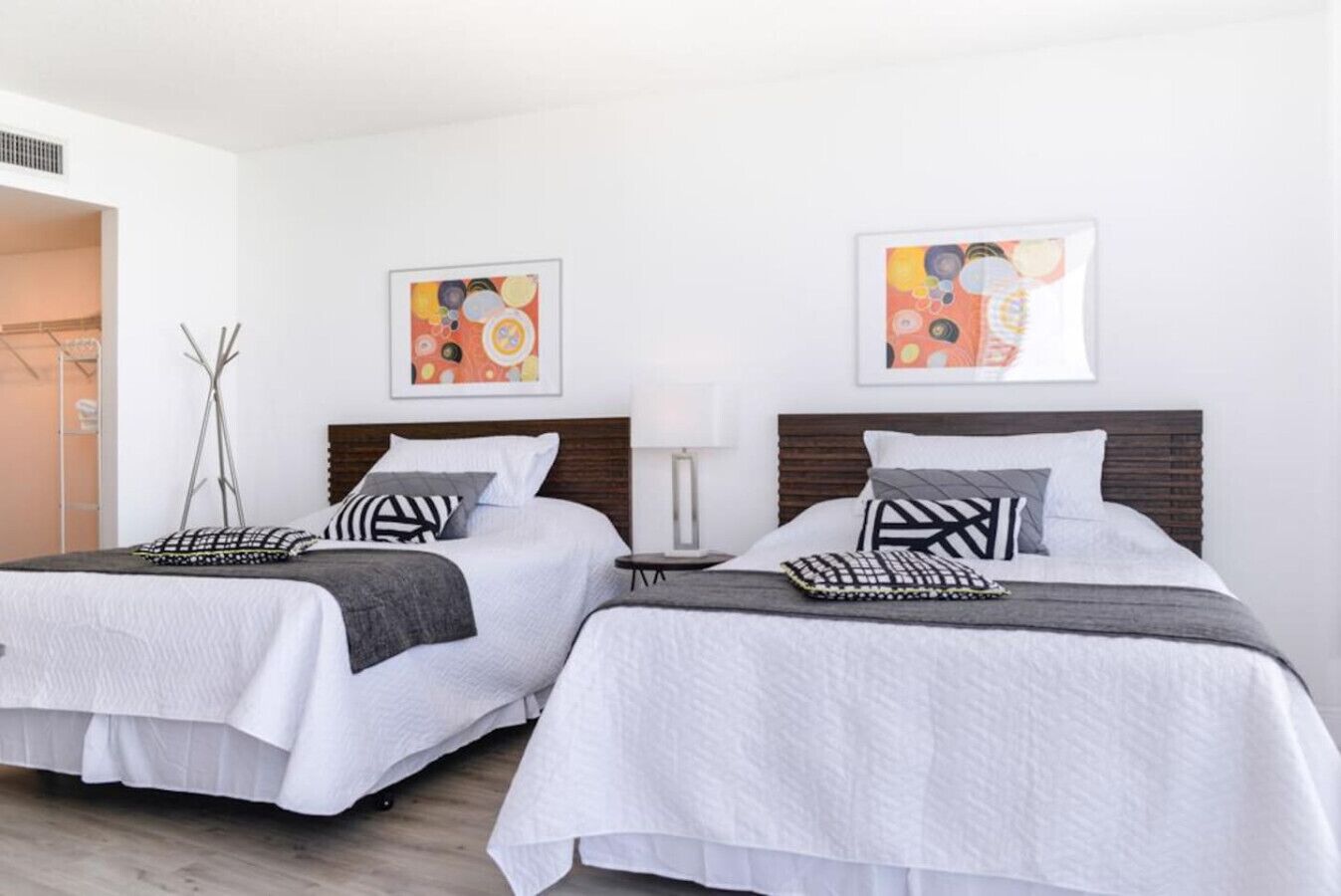 Une chambre d’hôtel avec deux lits, du linge de lit blanc et des œuvres d’art abstraites accrochées aux murs.