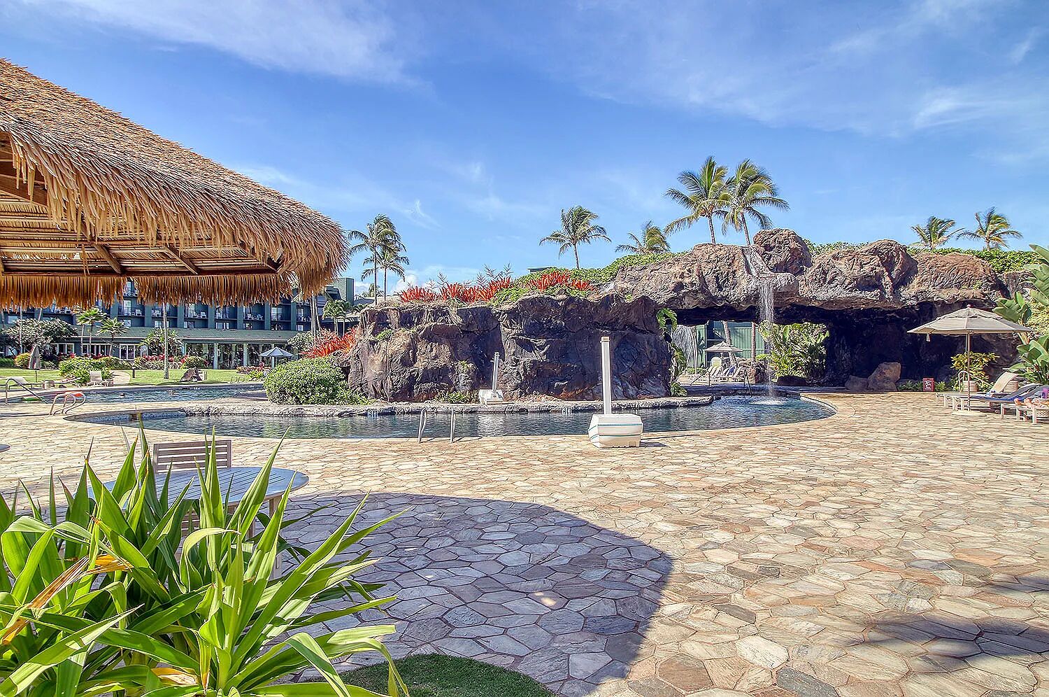 A hotel courtyard with a pool, palm trees, and a thatched-roof building.
