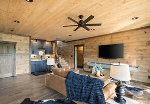 Un interior de cabaña de madera moderna con sala de estar, cocina y un televisor de pantalla plana montado en la pared.