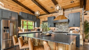 A modern kitchen with a large island, stainless steel appliances, and wooden beams. - Sippin on Sunsets: Ultra Luxe Escape • Epic Views • Hot-Tub • Secluded Comfort (Cherry Log)