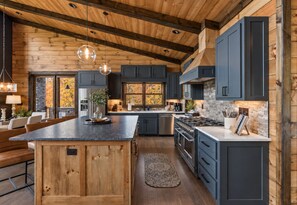 A modern kitchen with wooden beams, dark cabinets, and a central island. - Sippin on Sunsets: Ultra Luxe Escape • Epic Views • Hot-Tub • Secluded Comfort (Cherry Log)