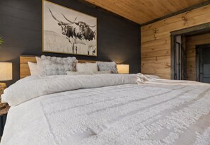 Un dormitorio con una cama grande, cabecera con almohadones, una obra de arte en la pared de un toro y paneles de madera.