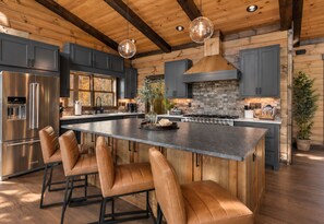 A modern kitchen with a large island, stainless steel appliances, and wooden accents. - Sippin on Sunsets: Ultra Luxe Escape • Epic Views • Hot-Tub • Secluded Comfort (Cherry Log)