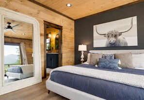 A bedroom with a large bed, a ceiling fan, a mounted painting of a yak, and a view through a window.