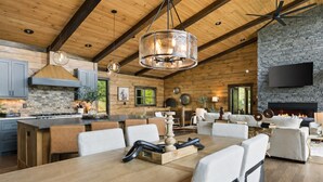 A spacious kitchen with a central island, wooden ceiling beams, and a stone fireplace. - Sippin on Sunsets: Ultra Luxe Escape • Epic Views • Hot-Tub • Secluded Comfort (Cherry Log)