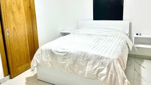Quarto com uma cama, guarda-roupa de madeira, mesa de cabeceira branca, porta preta e aparelho de ar condicionado branco.