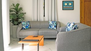 Uma sala de estar com um sofá cinzento, duas poltronas a combinar, uma mesa de centro de madeira e um vaso com planta.