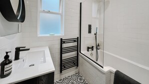 Uma casa de banho moderna com lavatório branco, suporte de toalhas preto e cabine de duche com paredes de vidro.