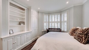 Quarto com cama grande, estantes embutidas e janela saliente com persianas.