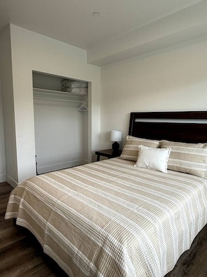 Un dormitorio con cama, mesita de noche, lámpara, armario y suelo de madera.