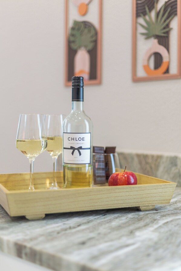 Une bouteille de vin Chloe Pinot Grigio sur un plateau en bois, accompagnée de deux verres et d’une pomme.