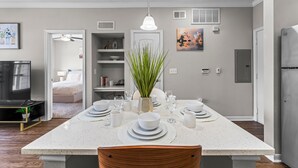 A modern kitchen with a central island, white countertops, and a dining area set for four. - 1BR Near The Woodlands Pool, Gym & Free Parking (Magnolia)