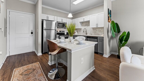 A modern kitchen with white cabinetry, a central island, stainless steel appliances, and a bar stool. - 1BR Near The Woodlands Pool, Gym & Free Parking (Magnolia)