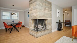 A dining area with a stone fireplace, a chandelier, and a dining table with chairs.