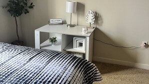 Une chambre à coucher comprenant un lit, une table de chevet, une lampe, une plante, un élément de décoration murale et une prise de courant.